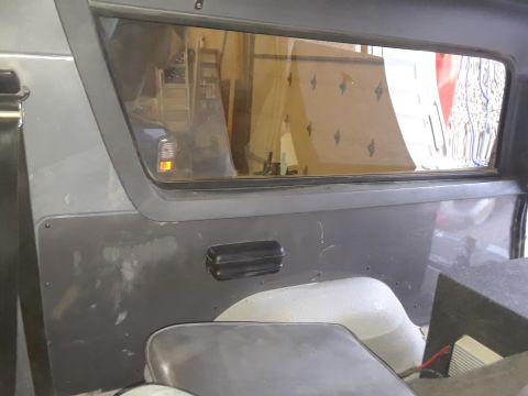 1985 Ford Bronco - Interior view of a vehicle's side paneling and window, with a black grab handle visible.