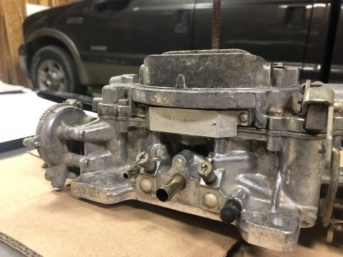 1980 Ford Bronco - A carburetor is shown in focus, with a vehicle partially visible behind it.