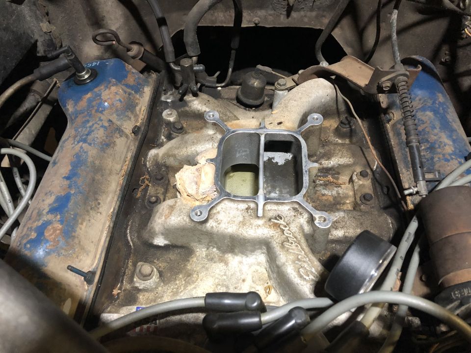 Engine intake manifold with carburetor mounting plate removed, showing dirt and grime