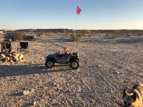 1992 Jeep Wrangler - Child driving a toy Jeep Wrangler in a desert setting with camping gear visible.