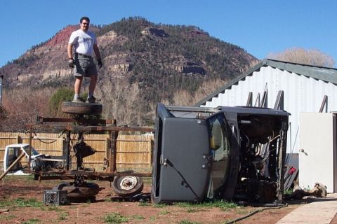 1990 Ford Bronco - Overturned vehicle and man on metal frame with a mountain backdrop.
