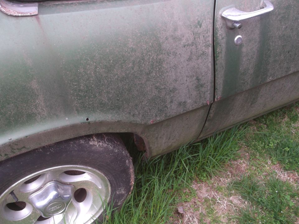 Green 1972 Ford Maverick side view showing fender, door, and wheel. The car has a chrome door handle and appears weathered