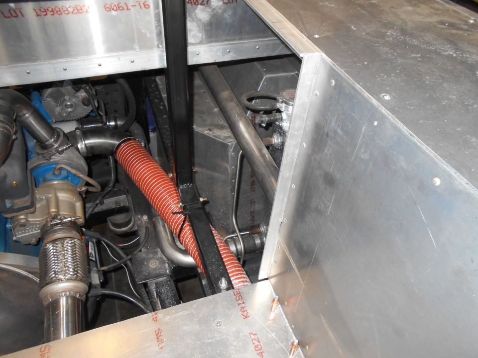 Engine compartment with aluminum panels, red hose, and exhaust components