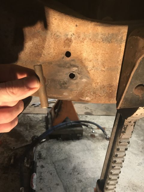 1984 Ford Bronco - Close-up view of a rusty vehicle frame section with a hand holding a metal rod, possibly during a repair or modification.