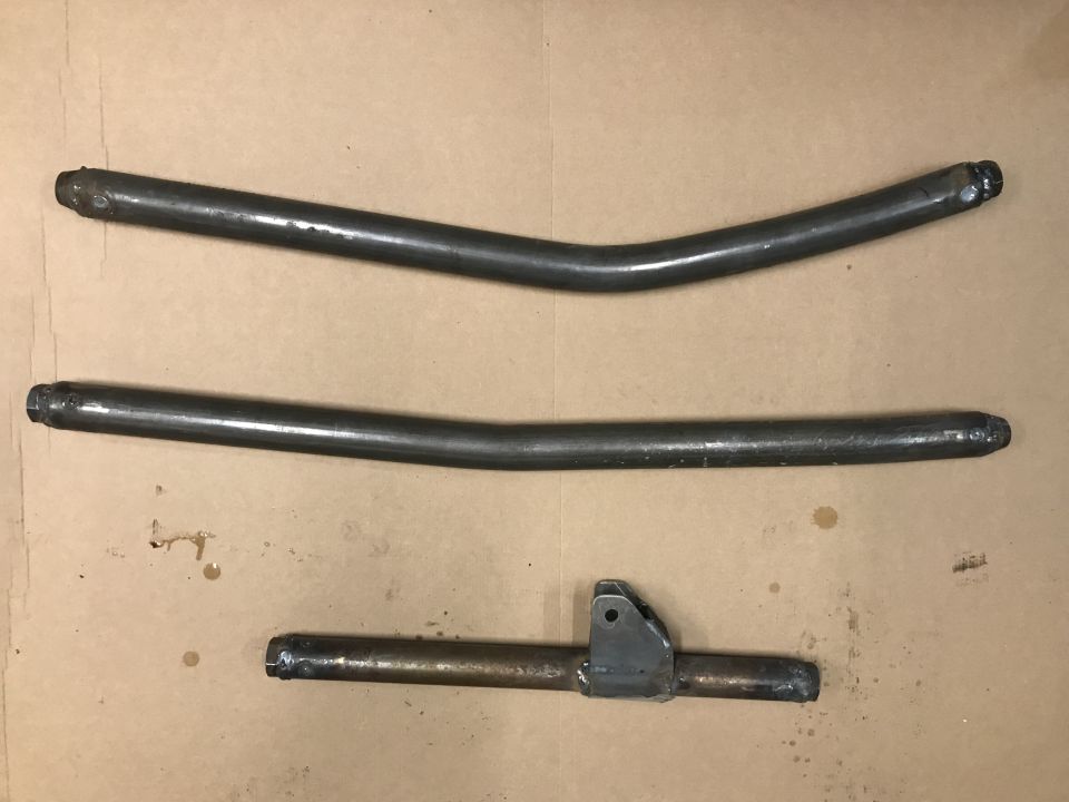 Three metal pipes, two curved and one straight with a bracket, laid out on a brown surface. Supermotors.net logo visible