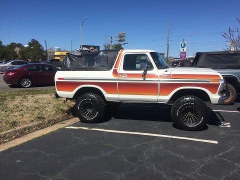 1979 Ford Bronco - This 1979 Ford Bronco features a distinctive orange and white stripe pattern and a removable soft top, parked in a lot.