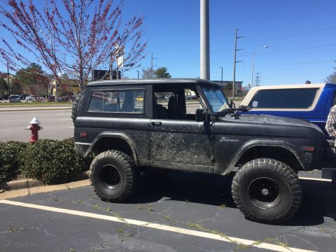 1979 Ford Bronco - A dirty black Ford Bronco is parked in a lot next to another Bronco.
