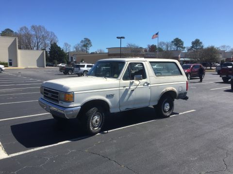 1979 Ford Bronco - White Ford Bronco parked in a lot with other vehicles and buildings visible.