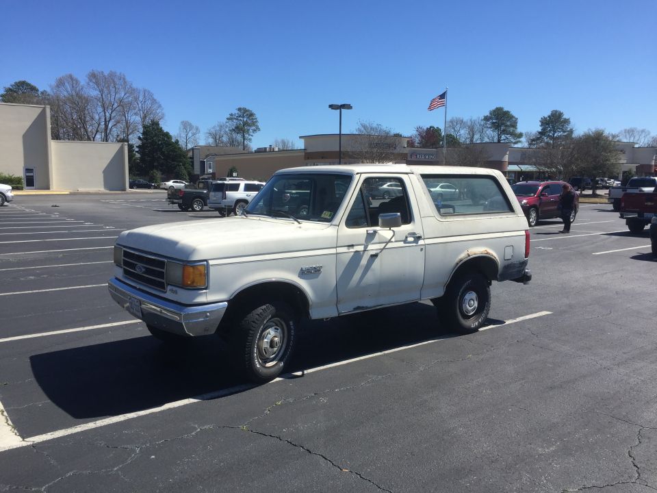 White Ford Bronco parked in a lot, side view. Other vehicles and buildings in background