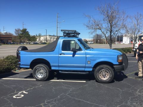 1979 Ford Bronco - A blue Ford Bronco is parked in a lot under a clear sky, showing its side profile and front end.