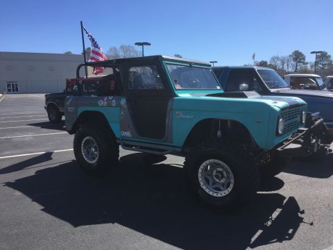 1979 Ford Bronco - A modified Ford Bronco is parked in a lot under a clear blue sky, with an American flag flying from a rear-mounted pole.
