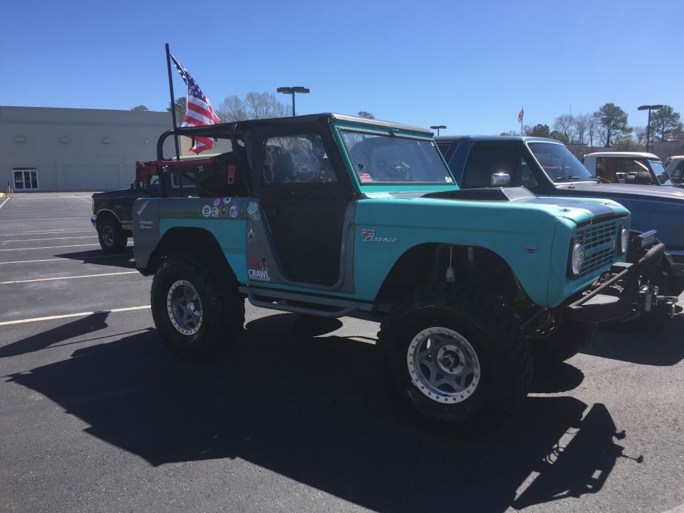 Teal Ford Bronco with an American flag on a pole, parked next to another vehicle