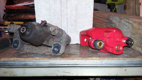 Old rusty brake caliper next to a new red brake caliper