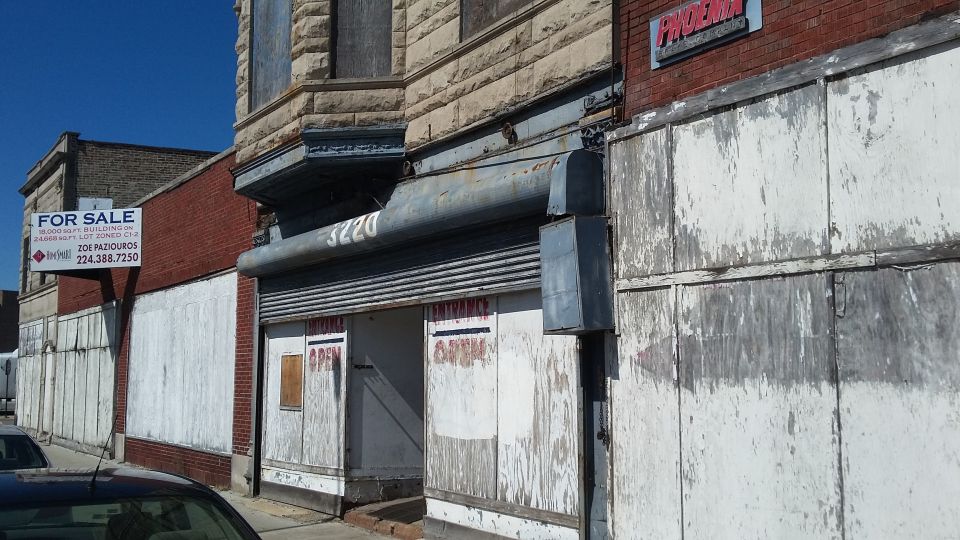 Abandoned storefront with boarded windows and peeling paint. A 'For Sale' sign is visible on the left
