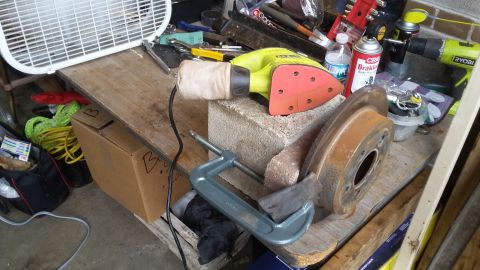 Workbench with a sander, C-clamp, and rusty brake rotor