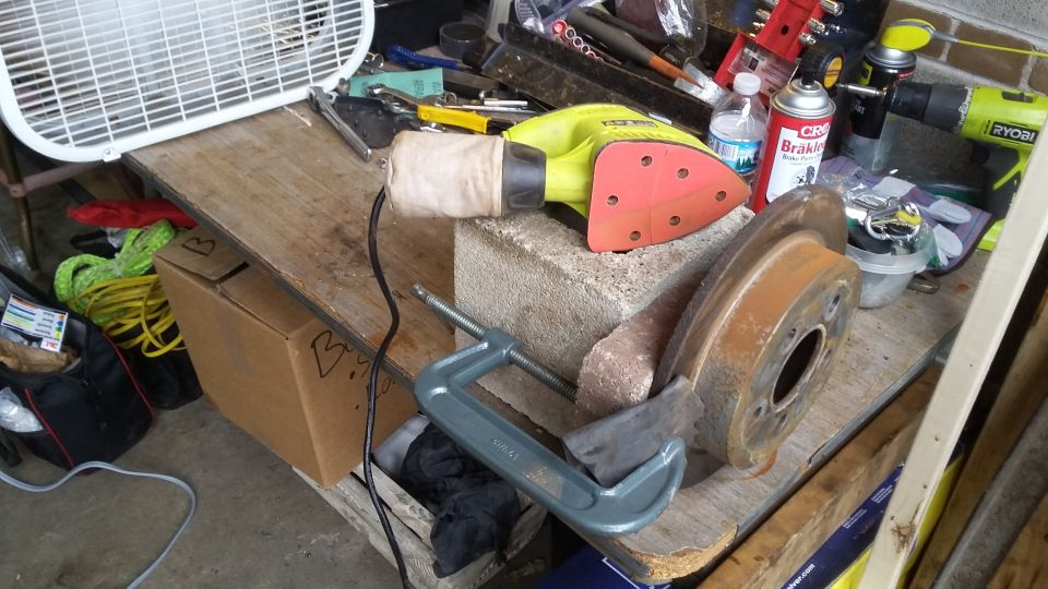 Workbench with a sander, C-clamp, and rusty brake rotor