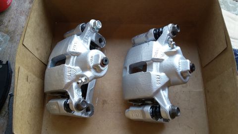 Two silver brake calipers sitting in a cardboard box