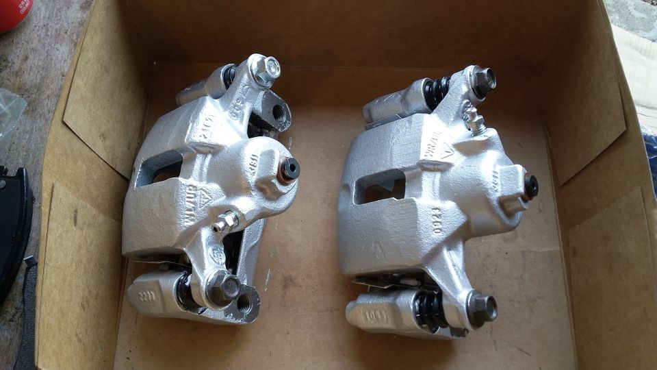 Two silver brake calipers sitting in a cardboard box