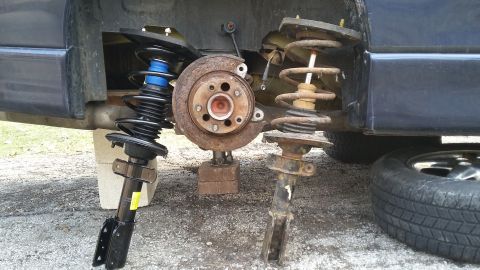 Front suspension hub exposed with old and new strut/coil-spring assemblies on the ground