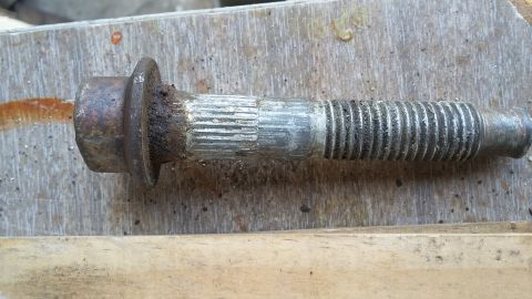 Rusted lug bolt with a flanged head and splined shaft, lying on a wooden surface