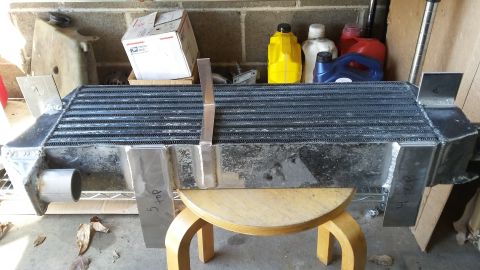 Intercooler with metal brackets and inlet/outlet pipes, resting on a wooden stool