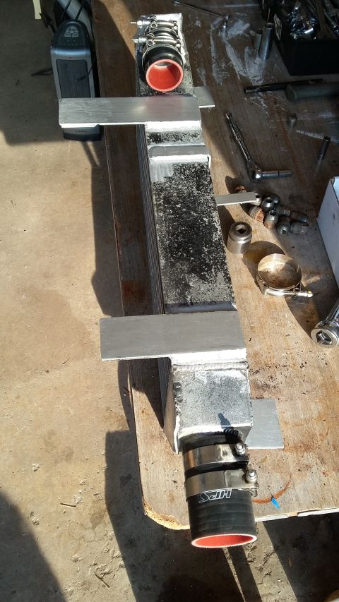 Intercooler with red-lined hoses and aluminum mounting brackets on a workbench