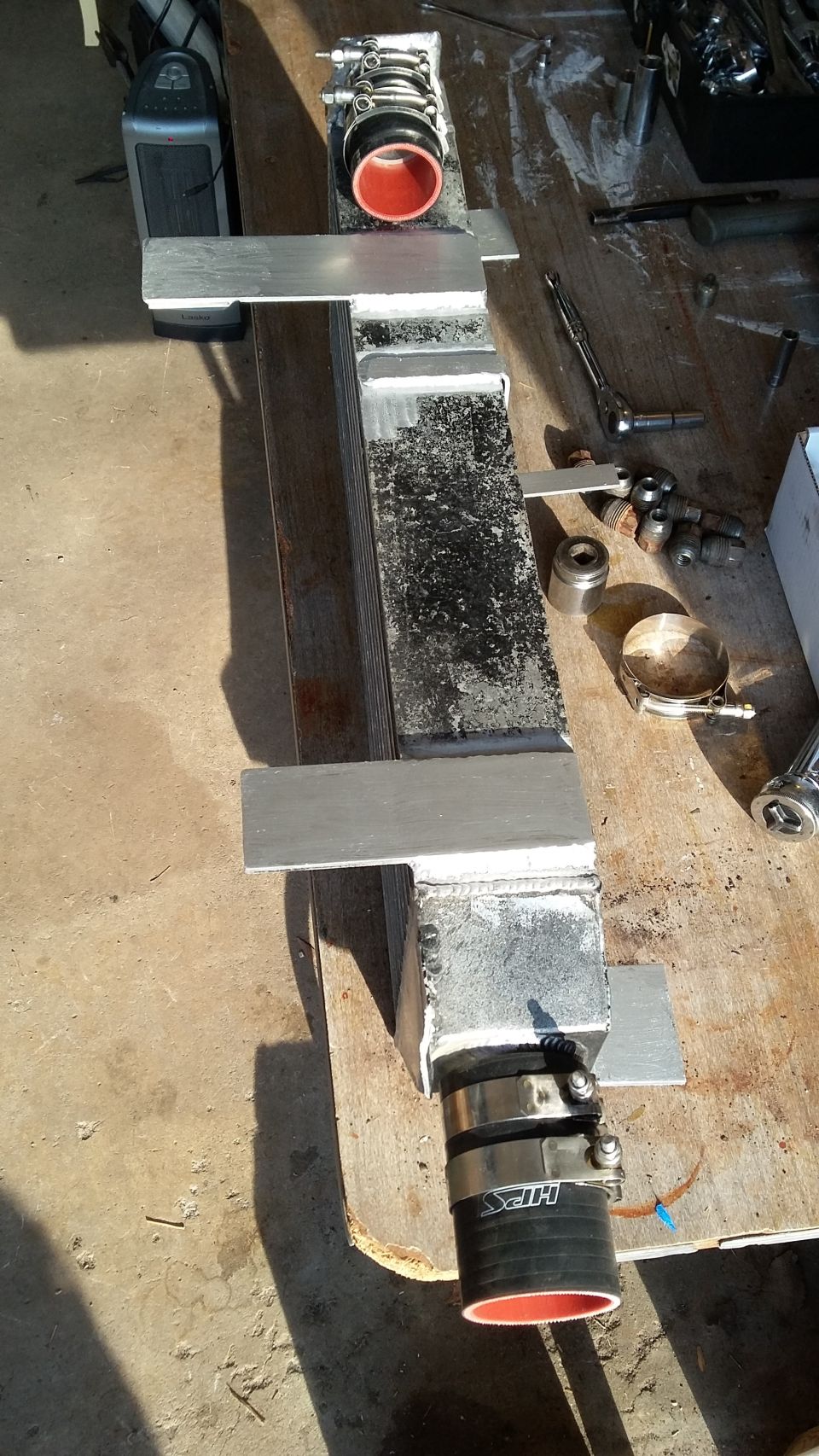 Intercooler with red-lined hoses and aluminum mounting brackets on a workbench