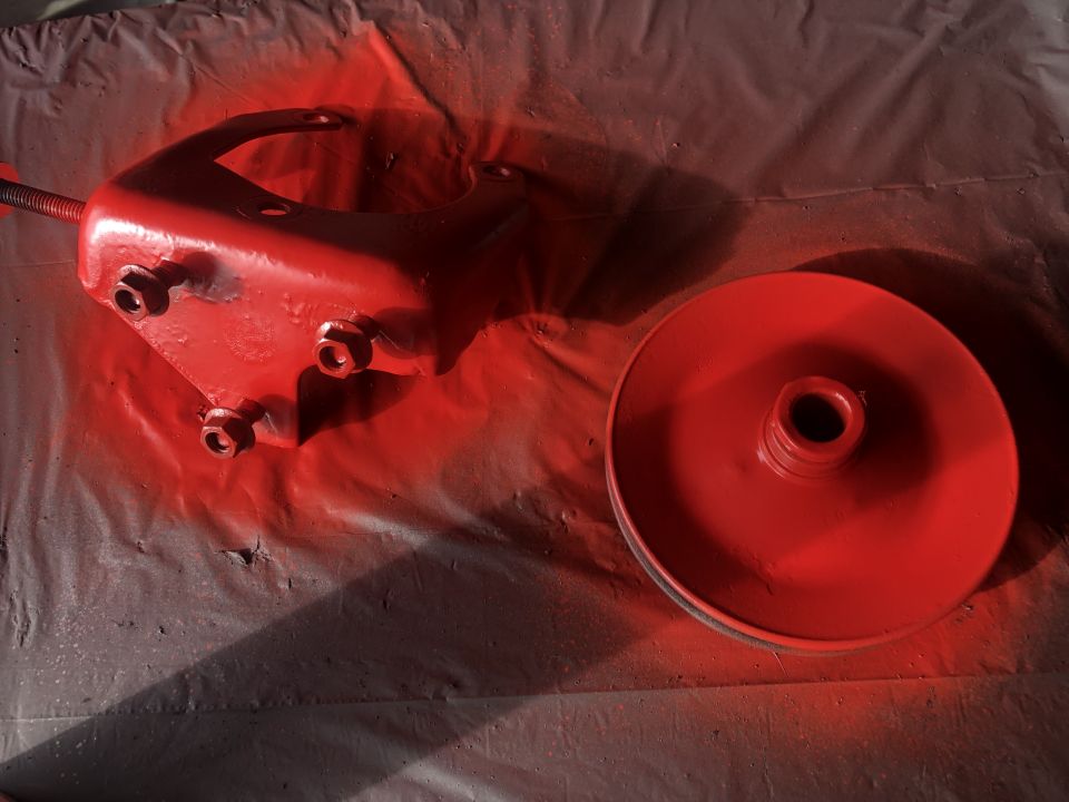 Two red painted metal automotive parts on a drop cloth