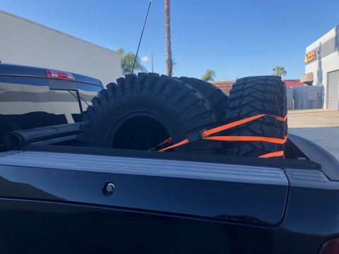 1992 Jeep Wrangler - Off-road tires are strapped down in the bed of a black pickup truck.