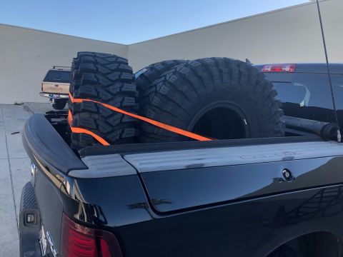 1992 Jeep Wrangler - Off-road tires are strapped down in the bed of a black pickup truck, with another vehicle in the background.