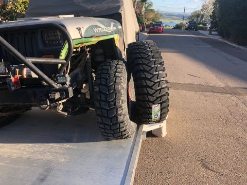 1992 Jeep Wrangler - A Jeep Wrangler's front tire and fender are visible on a tow truck ramp, with a scenic overlook in the background.