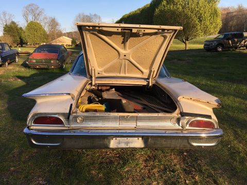 1960 Ford Starliner - The distinctive tail fins and chrome bumper of a 1960 Ford Starliner are visible with the trunk open, revealing stored items.