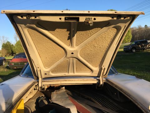 1960 Ford Starliner - Trunk of a 1960 Ford Starliner open, revealing stored items and other vehicles in the background.