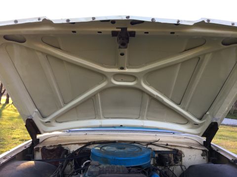 1960 Ford Starliner - The engine bay of a white 1960 Ford Starliner is visible with the hood raised, revealing the engine and air cleaner.