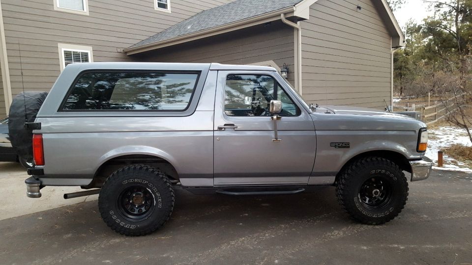 Side view of a 1995 Ford Bronco parked in a driveway. It has a spare tire mounted on the rear
