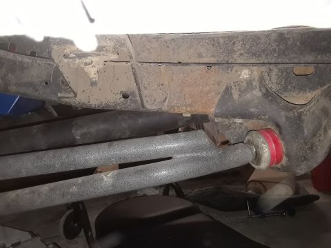 1985 Ford Bronco - Close-up view of red suspension bushings attached to gray metal bars beneath a vehicle's frame.