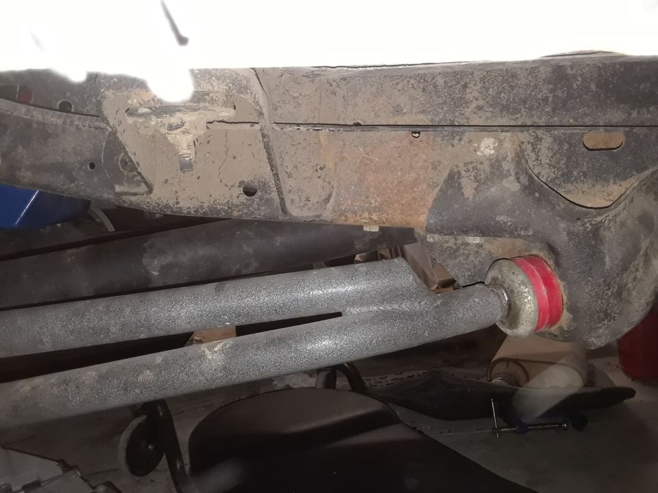 Red suspension bushings on gray metal bars under a vehicle frame
