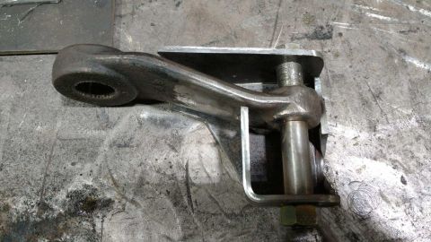 1984 Ford Bronco - A close-up view of a metal steering linkage component resting on a textured surface.