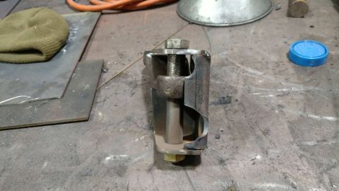 1984 Ford Bronco - A metal bracket assembly with a bolt is shown on a workbench.