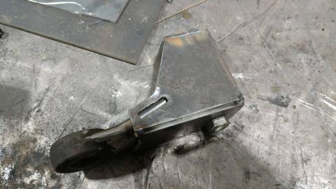 1984 Ford Bronco - A metal bracket with a bolt is shown on a workbench, possibly a custom part.
