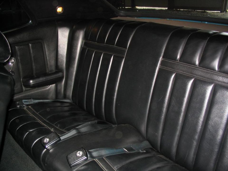 Black vinyl rear bench seat of a coupe with center armrest and seatbelts, two-door interior
