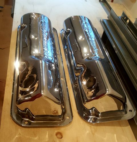 1973 Ford Mustang - Chrome valve covers with Ford branding are displayed on a wooden surface, with metal shelving in the background.
