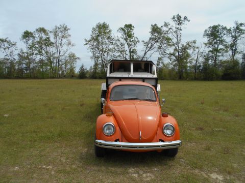 1992 Ford Bronco - An orange Volkswagen Beetle is seen from the front, towing a white camper trailer in a grassy field.