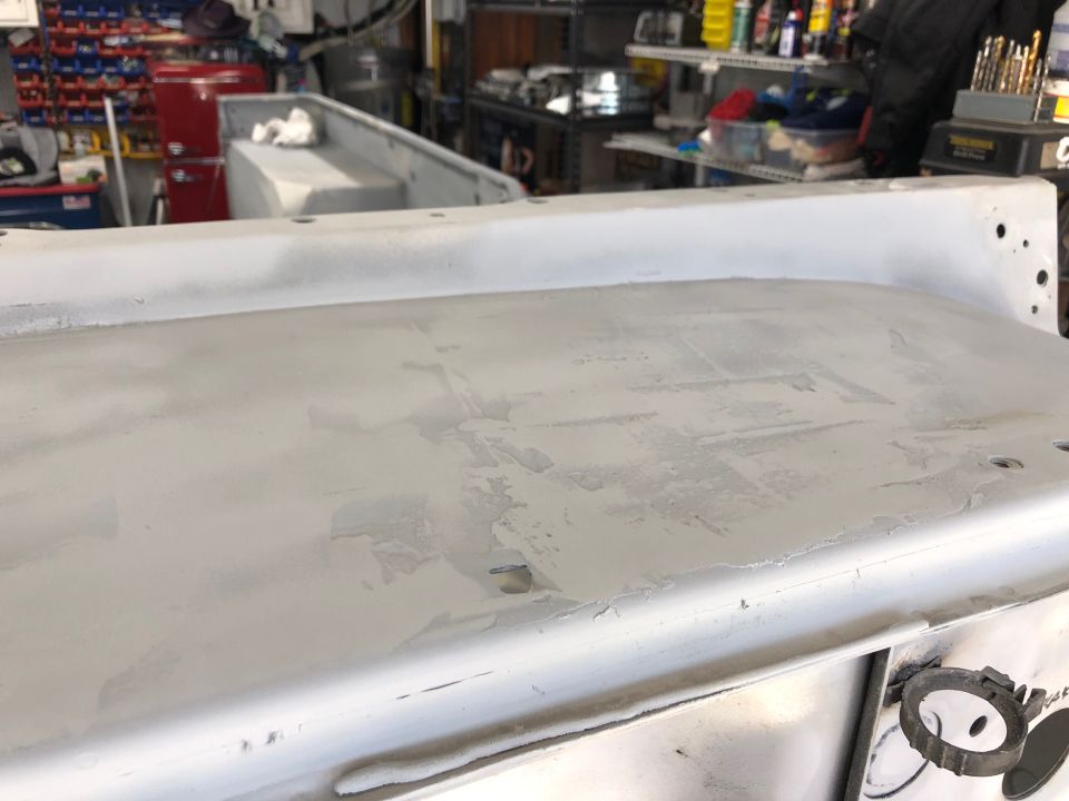 Close-up of a gray primed Jeep tub section with some rough patches, in a garage setting