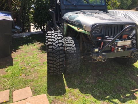1992 Jeep Wrangler - A Jeep Wrangler is parked on grass, displaying its large off-road tires, with one tire appearing wider than the other.