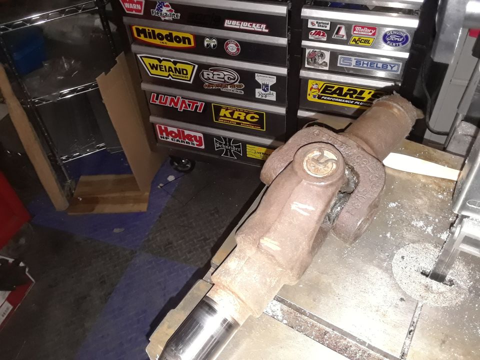 Driveshaft U-joint with rust and wear, resting on a metal surface near a band saw