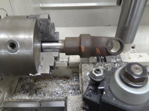 1985 Ford Bronco - A driveshaft component is held in a lathe chuck, undergoing machining with metal shavings accumulating around the work area.