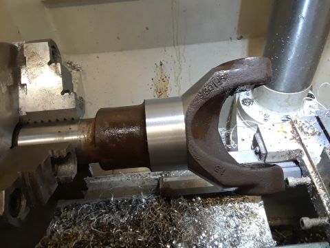 1985 Ford Bronco - A driveshaft yoke is clamped in a lathe, undergoing machining with metal shavings accumulating around the workpiece.
