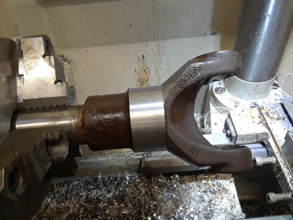 Driveshaft yoke being machined on a lathe, metal shavings around the chuck