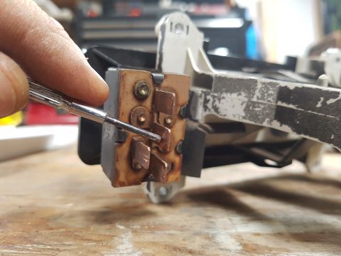 1978 Ford Bronco - A hand uses a screwdriver to adjust a component on a vehicle part, likely for repair or maintenance.